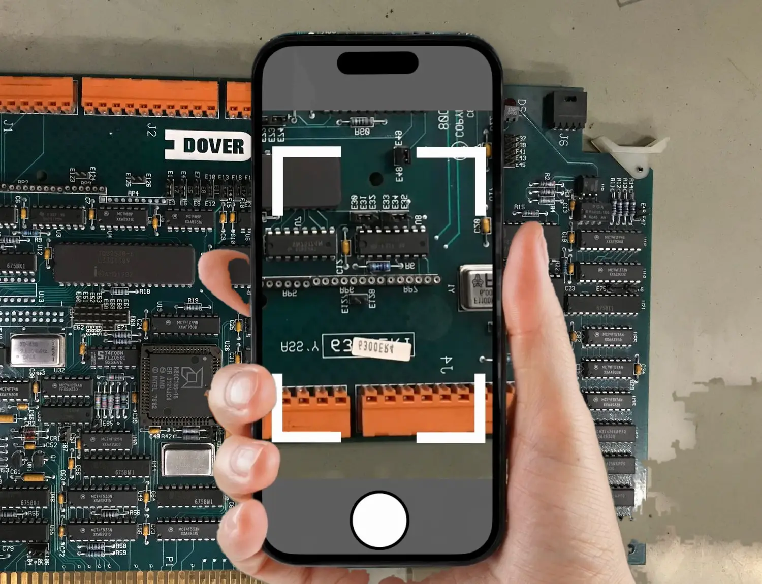 A mechanic holds the phone over a Dover circuit board and Zip Repair finds the part